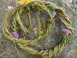 Zwei kleine, aus Weinranken geflochtene Kränze verziert mit gelben und lila Wiesenblumen.